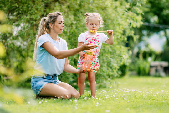 A little girl and her mother blow soap bubbles on a blurry background in a park or garden. A loving and happy family