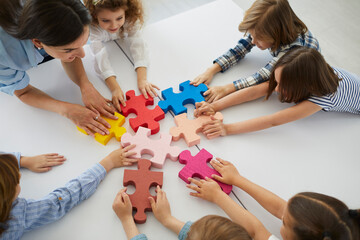 Team of elementary school children together with teacher join colorful jigsaw puzzle pieces...
