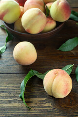 Fresh harvest of peaches in a clay bowl on a wooden rustic table. Peach leaves are present in the composition.