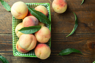 Naklejka na ściany i meble Ripe peaches in a basket on a wooden background. Peach leaves are scattered across the tabletop.