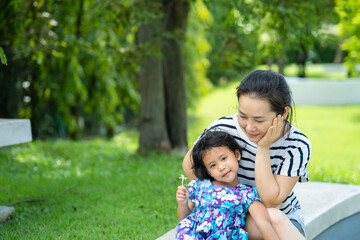 Happy little girl sitting with young mother on marble seat outdoor.