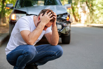 Young white man driver in car accident and holding his head near broken car on the road after a car accident. Caucasian man facepalm holding head injury after accident