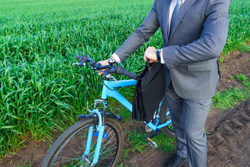 Businessman with a bicycle looking at his wristwatch in a green grass field - business concept for...