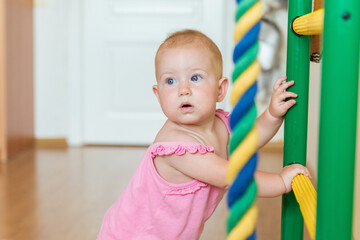 Cute baby performs gymnastic exercises on home sports complex stairs. Children's sports exercises. Physical education of children at home