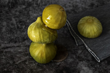 Composition of fresh green figs, one on top of the other, stacked, with honey falling on them until it falls at the base, all on a dark background of gray tones.