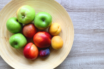 Wooden bowl with various colorful fruit on dark background. Top view.