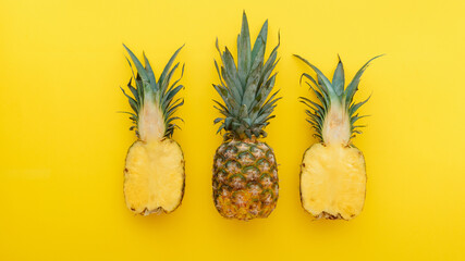 Pineapple fruit on yellow summer background. A whole tropical pineapple and half fruit in a minimalist style on a summer bright yellow background. Long web banner Flat lay