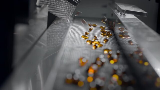 Yellow gel capsules move on the conveyor belt of the automatic medical machine. Production of dietary supplements and medicines. Medical plant for the creation of vitamin pills and mineral complexes.