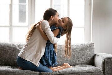 Happy young Caucasian mother relax on couch at home hug cuddle with small cute teen daughter....
