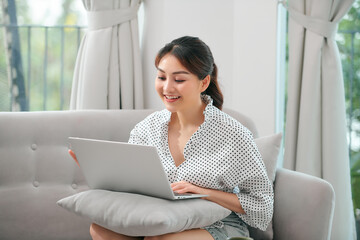 A asian woman spending time at home, sitting on sofa, using her laptop