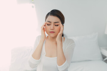 Young woman with headache, she is sitting on the bed and touching her temples