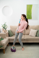 Happy woman cleaning home, singing at mop like at microphone and having fun,
