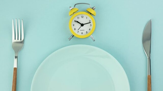 Intermittent fasting, diet, lunch time concept. Yellow alarm clock, empty plate and cutlery.
