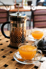 Close up view on french press and cups with sea buckthorn tea on the table.