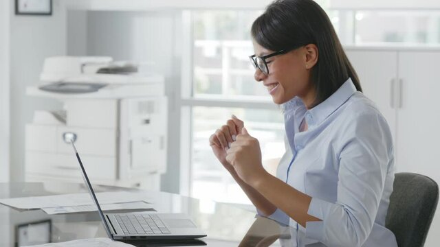 Happy african american businesswoman sitting at desk typing on laptop in contemporary office.