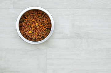 Dry pet food in a metal bowl on white wooden floor.