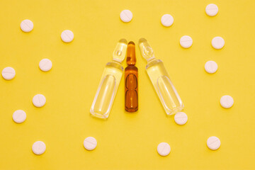 Transparent ampoules with liquid medicine are on yellow background around tablets which form polka...