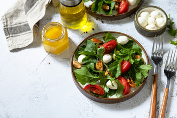 Healthy diet salad with arugula, mozzarella, mussels and vinaigrette dressing on a gray stone tabletop. Copy space.
