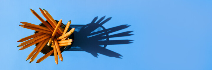 Graphite pencils in a metal grid-container on the office table top view on blue background.