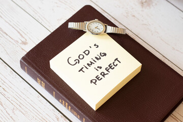 God's timing is perfect. Trust God and Jesus Christ. Have faith in His promises. Be patient. Holy Bible with inspiring handwritten note with a watch. Biblical concept.