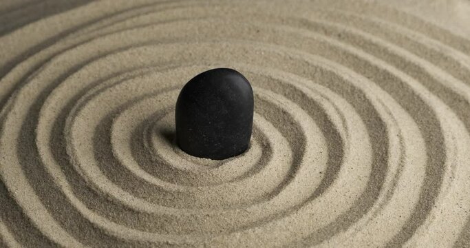 Rotation of the black stone in the center of the sand spiral. Close-up of patterns in the sand. Sand texture