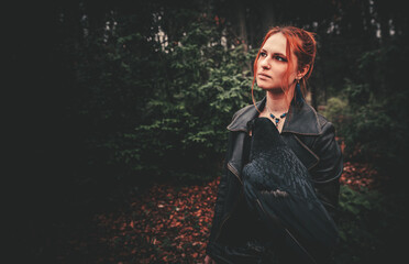 Fototapeta premium young woman or girl in the forest with a big black raven on his hand