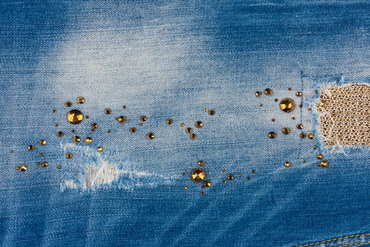 Trendy background. Ripped denim, embellished with rhinestones and gold thread.