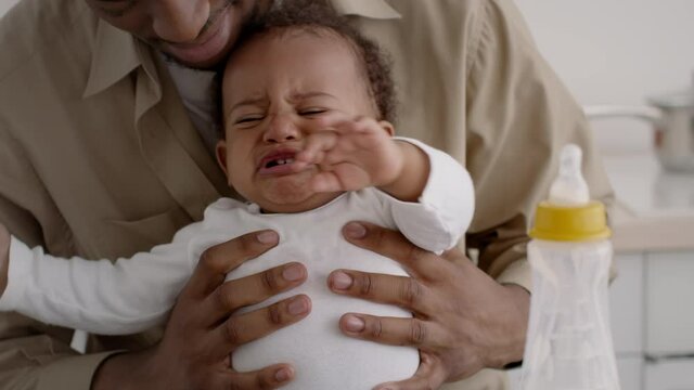 Close up portrait of sad african american baby boy crying in fathers hands, feeling stressed and annoyed, tracking shot