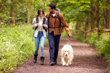 Couple With Pet Golden Retriever Dog Hiking Along Path Through Trees In Countryside