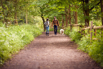 Fototapeta premium Couple With Pet Golden Retriever Dog Hiking Along Path Through Trees In Countryside