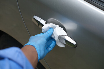 hand in blue gloves cleaning car door knob with tissue 