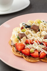 Heart waffle with banana and strawberry with gummy candy and ice cream on it.