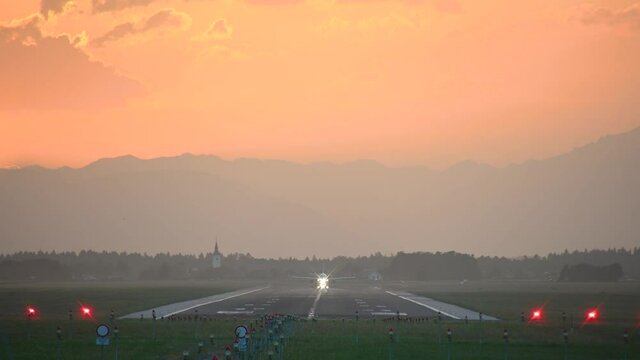 Large passenger airplane takes off. View of long runway, Ljubljana airport, Slovenia. Dramatic and colorful sunset. Aircraft taking off facing towards the camera. Static, real time