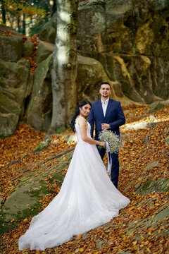 A groom and bride in wedding suits are posing in the forest. Autumn. Outdoor. Beautiful background. 