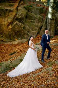A groom and bride in wedding suits are walking in the forest. Autumn. Outdoor. Beautiful background