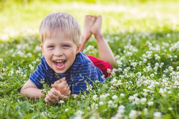 A happy, smiling boy is lying on a green grass lawn. Happy childhood, summer and outdoor recreation