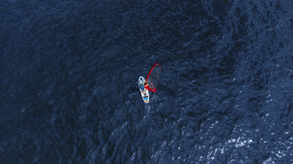 A man on an inflatable board with a sail in the middle of the water. Windsurfing. Top View