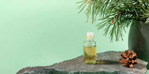 Glass bottle of essential pine oil on grey stone on mint green. Advertising banner.