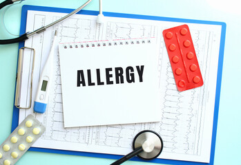 A notepad with the text ALLERGY lies on a medical clipboard with a stethoscope and pills on a blue background.