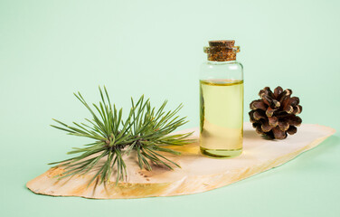 Essential pine oil in glass bottle on wooden saw cut on mint green background.