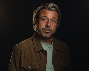 Middle-aged man with a stubble and blond hair wears a brown corduroy jacket with a light green t-shirt.