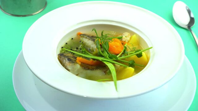 Fish soup - ukha. Lunch in a white deep plate. Fish food on the table. Potatoes, carrots, onions, broth. Fish meat Pike perch. The plate is spinning. Healthy and tasty. Restaurant serving
