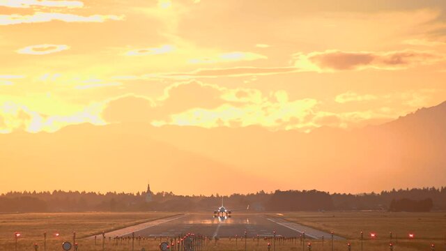 Large passenger airplane takes off. View of long runway, Ljubljana airport, Slovenia. Dramatic and colorful sunset. Aircraft taking off facing towards the camera. Static, real time