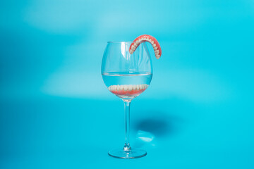 Dental prosthesis care. Full removable plastic denture of the jaws. A set of dentures in a glass of water on a blue background. Two acrylic dentures. Dentures or false teeth, close-up. Copy space