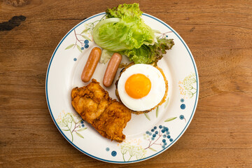Top view of thai style american fried rice with green vegetables, sausages, fried egg, fried chicken and raisin in white ceramic dish.