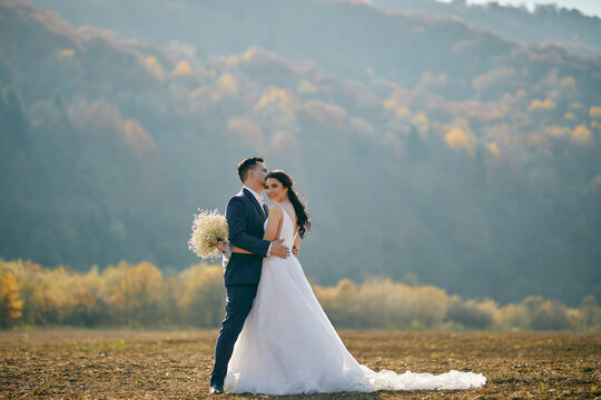 A beautiful young wedding couple embrace at the field with great view of hills. Outdoors. Nature