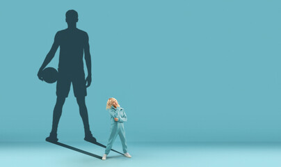 Conceptual image with boy and shadow of fit male basketball player on blue background. Childhood and dream about big and famous future.