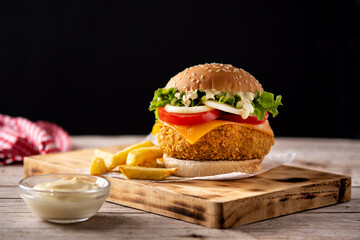 Crispy chicken burger with cheese and french fries on wooden table	