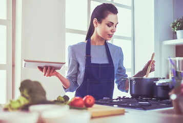 Young woman using a tablet computer to cook in her kitchen