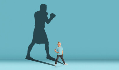 Childhood and dream about big and famous future. Conceptual image with boy and shadow of strong male boxer on blue background. Dreams, imagination, education concept.